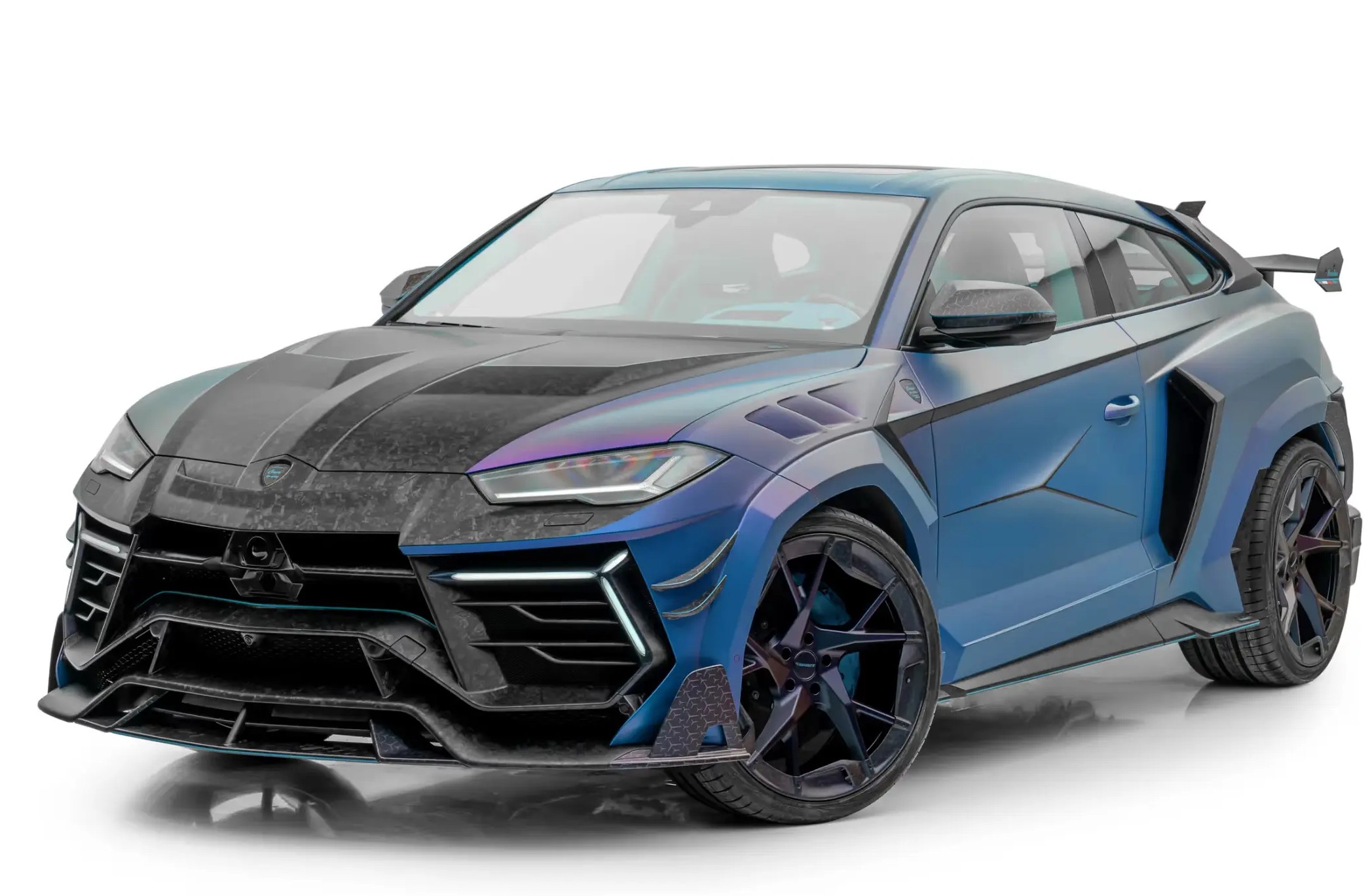 The image shows a Lamborghini Urus in black and dark blue with extensive carbon fiber details. Carbon fiber elements are visible on the front splitter, side skirts, mirror caps, and rear diffuser. The dark blue accents blend with the black body, creating a bold and performance-focused appearance. The vehicle looks sporty, exclusive, and highly customized.